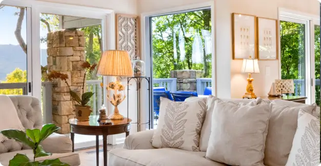 A cozy living room with large windows, beige couches, a wooden coffee table, and a high vaulted ceiling with exposed beams.